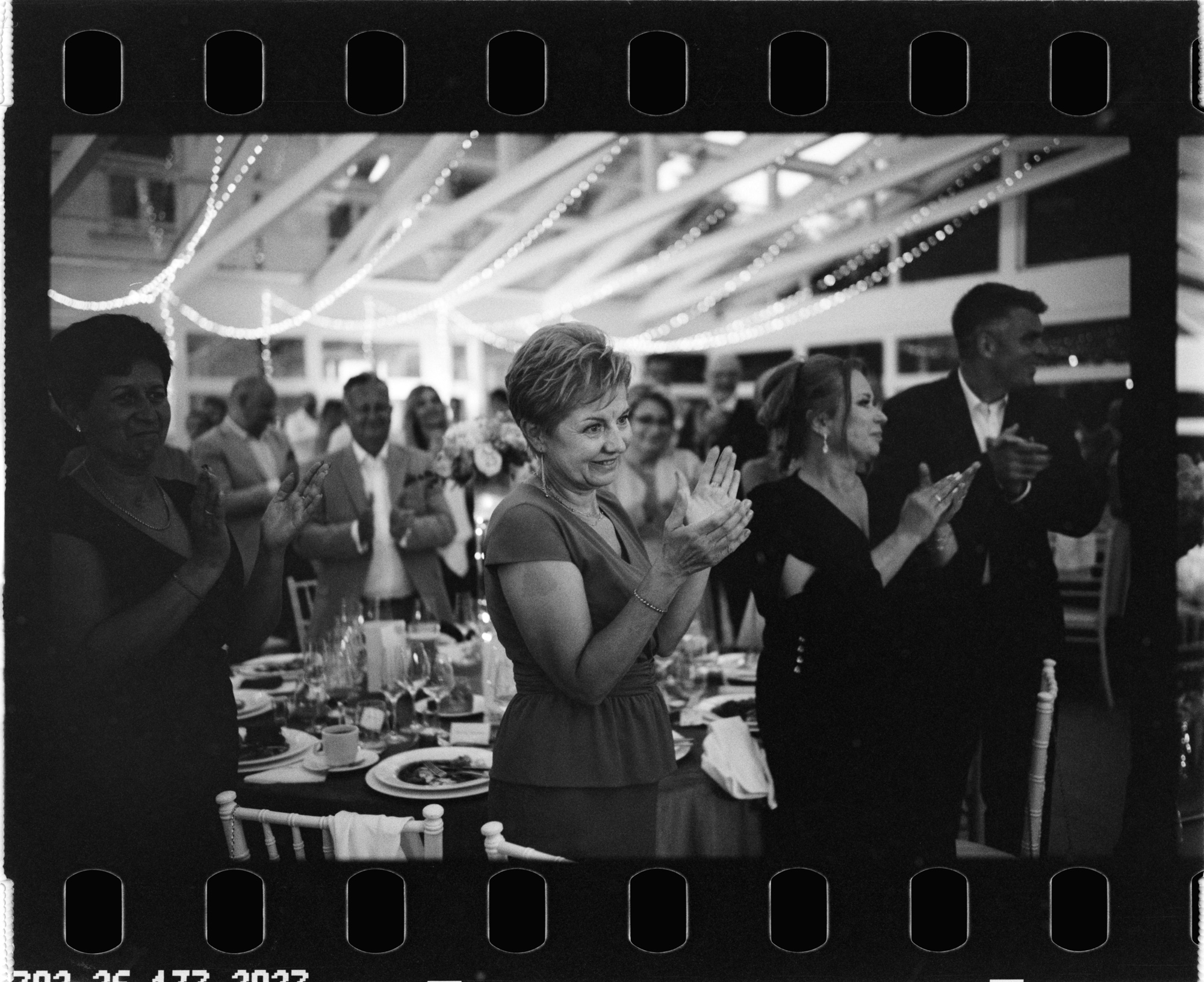 Uśmiechnięci goście biją brawo podczas przyjęcia. Fotografia na filmie Ilford HP5.