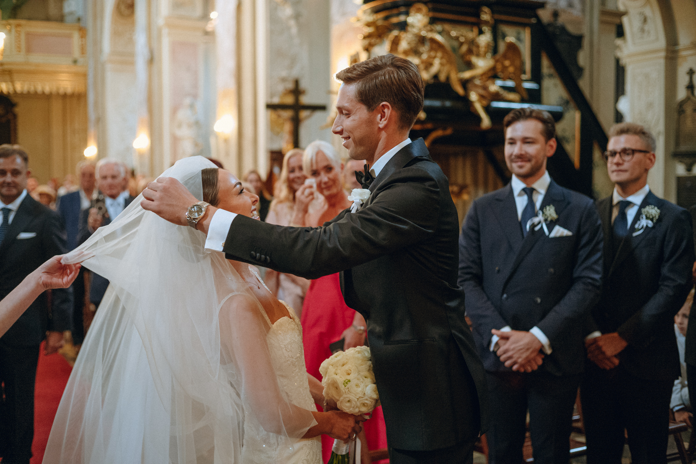 Pan młody odsłania welon panny młodej podczas ceremonii w kościele.
