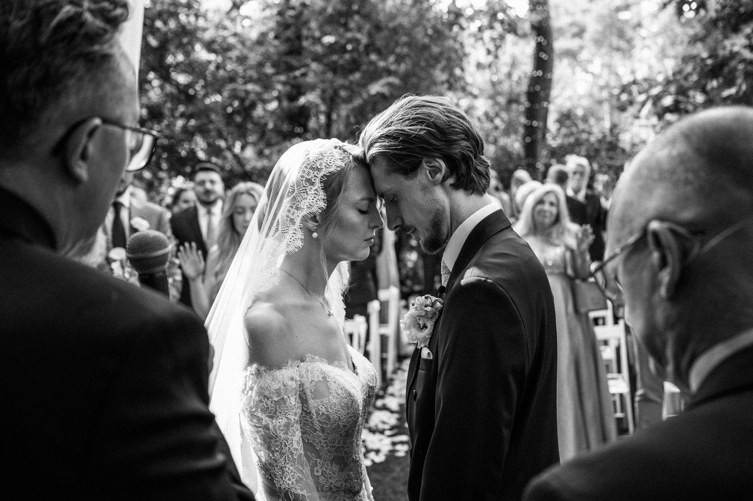 Para młoda dotyka się czołami podczas ceremonii w plenerze. Czarno-biała fotografia.