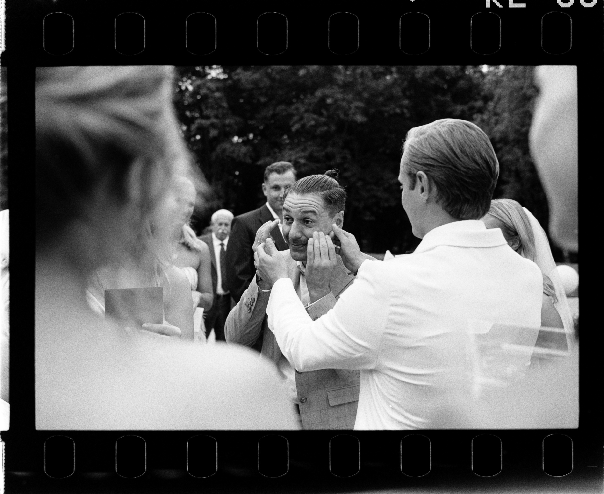 Goście rozmawiają z nowożeńcami podczas przyjęcia w ogrodzie. Fotografia na filmie Ilford HP5.
