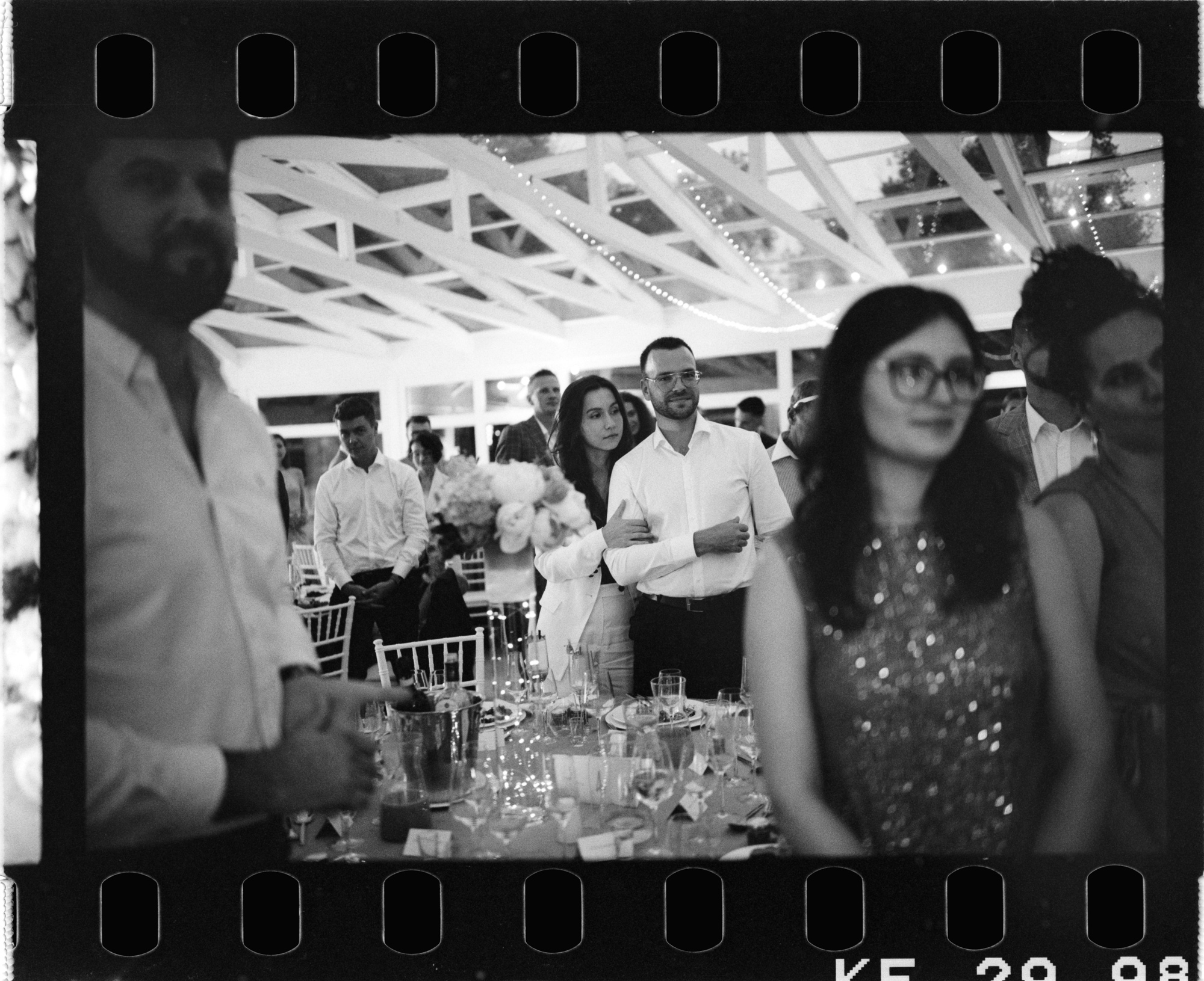 Goście stoją przy weselnym stole. Fotografia na filmie Ilford HP5.