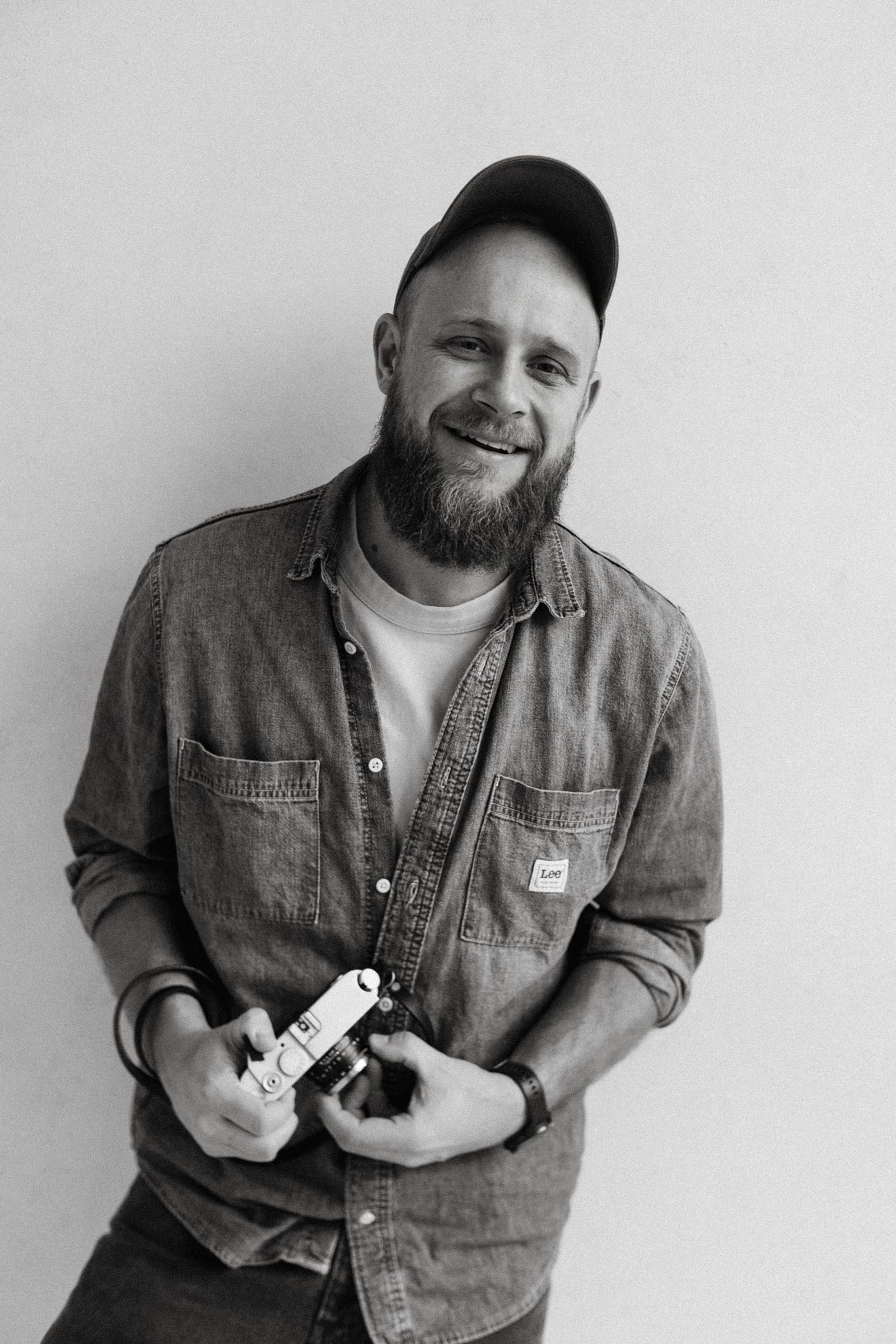Jacek Waszkiewicz z aparatem. Czarno-biały portret fotografa.