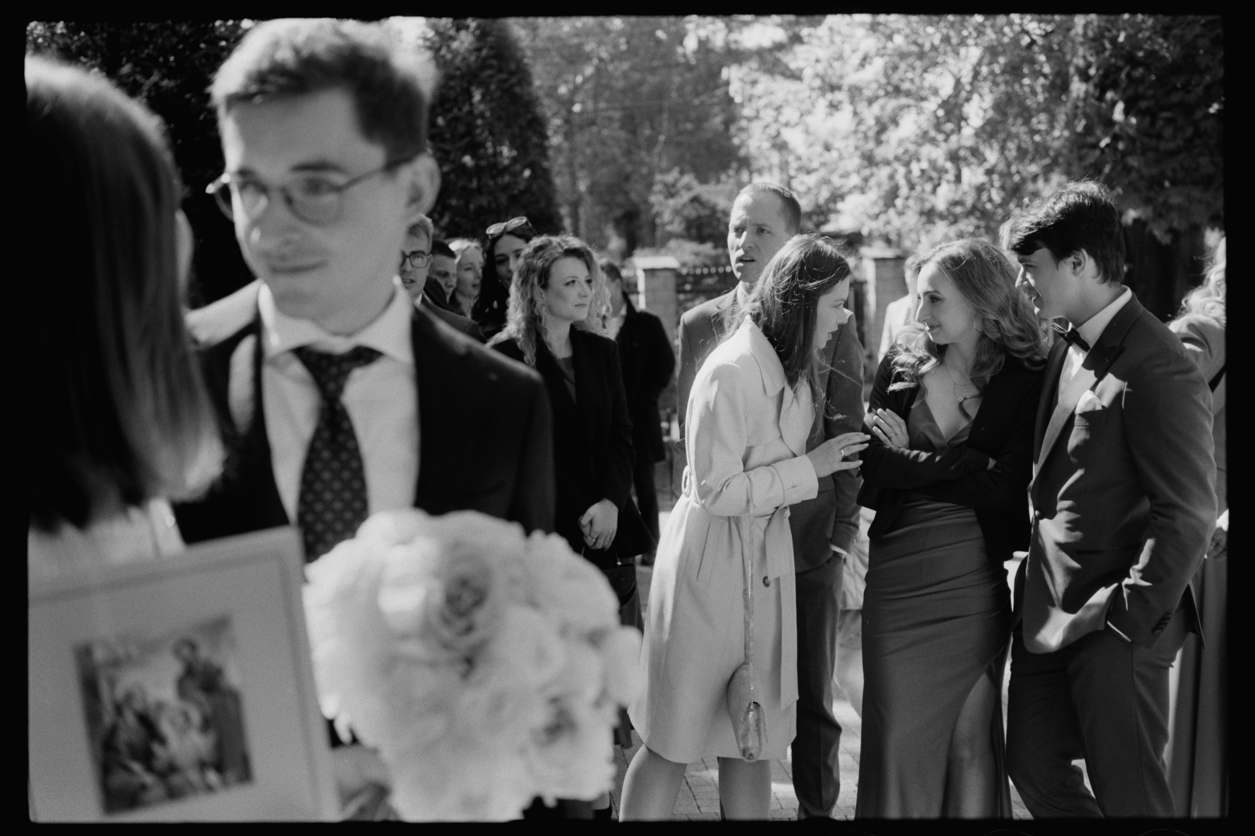 Goście rozmawiają w ogrodzie podczas ślubu. Skan negatywu Ilford HP5.
