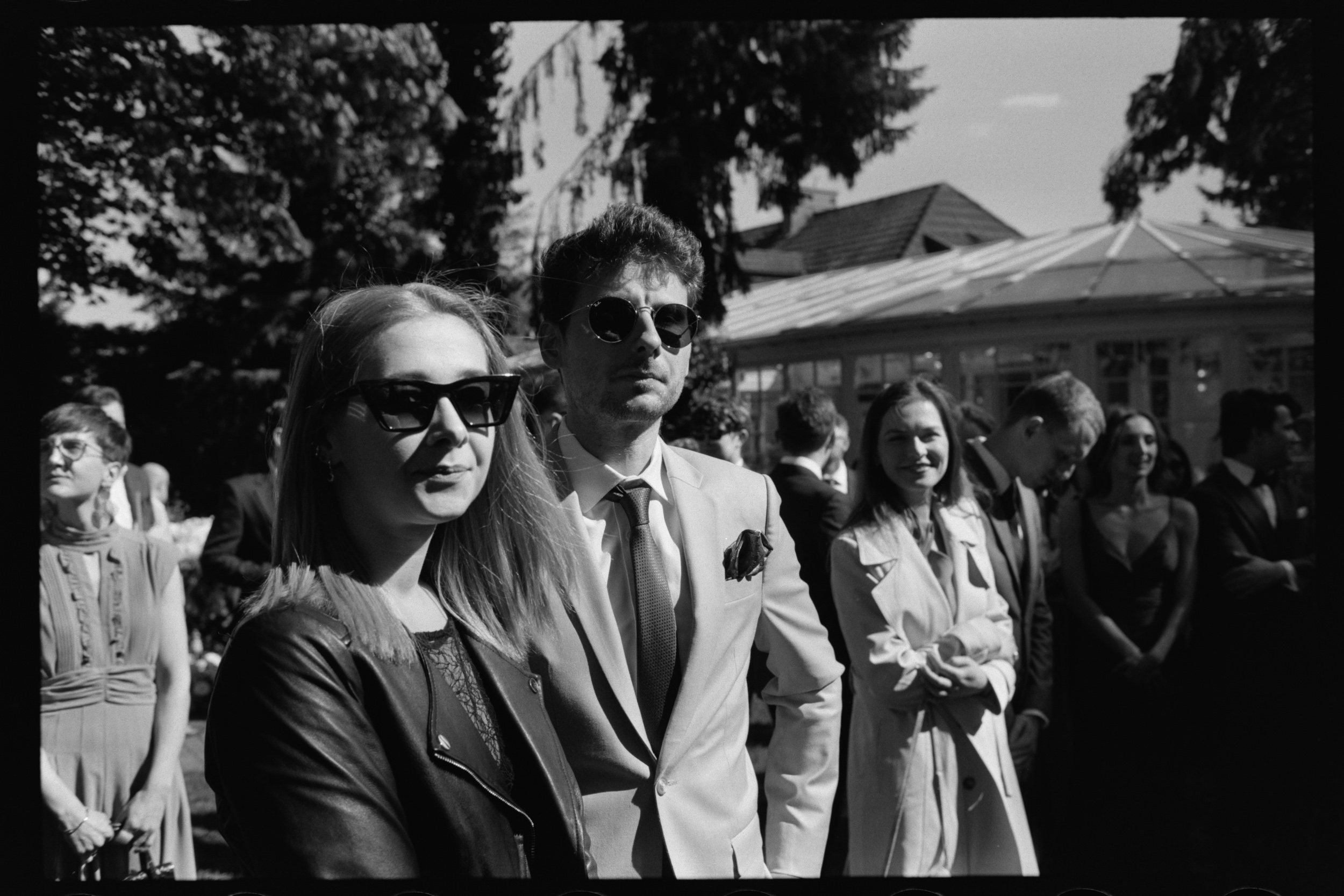 Para w okularach przeciwsłonecznych wśród gości weselnych. Skan negatywu Ilford HP5.