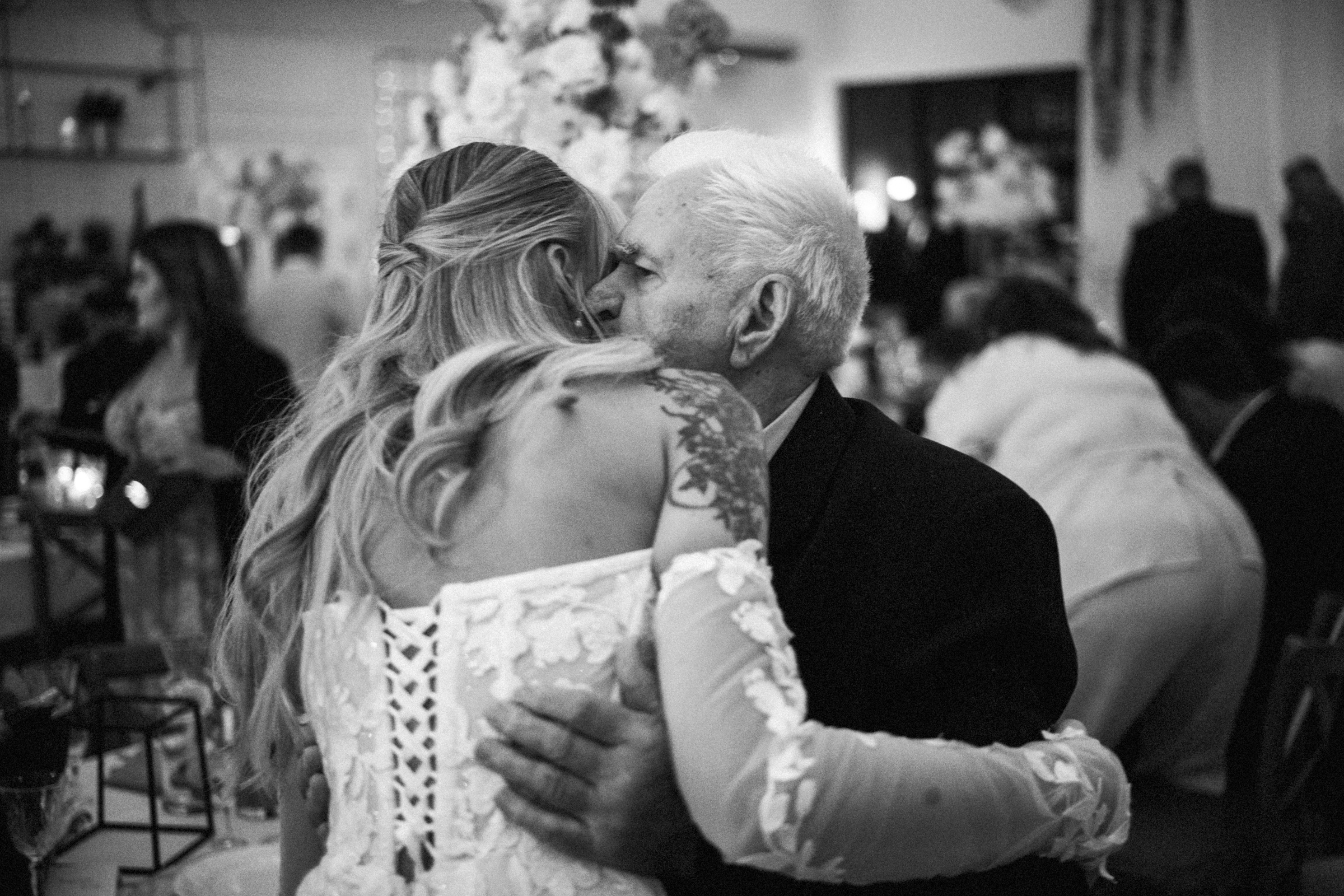 Panna młoda obejmuje starszego mężczyznę podczas przyjęcia. Czarno-biała fotografia.